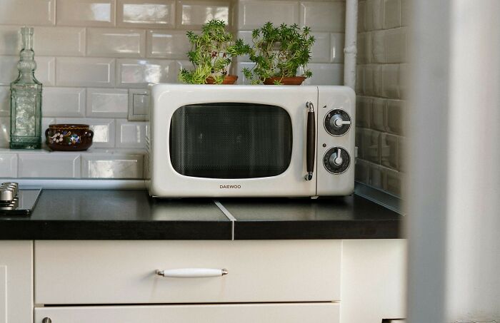 Retro white microwave on a kitchen counter with small plants on top, illustrating tiny human mistakes in history.
