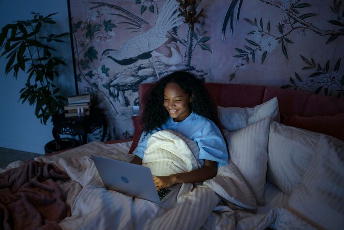 Woman in bed using laptop at night, surrounded by pillows and blankets, exploring terrifying things people swear they've seen.