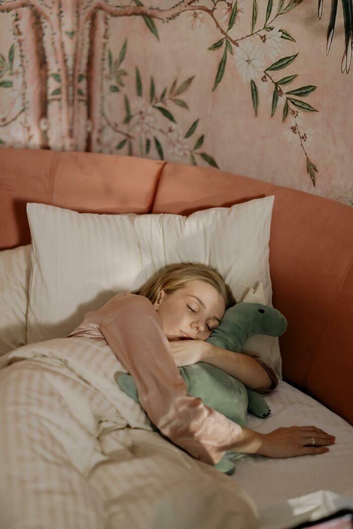 Woman sleeping peacefully in bed hugging a stuffed dinosaur, illustrating heartwarming and harmless secrets.