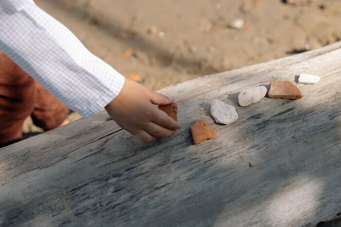 Child's hand arranging stones on weathered wood, evoking creepy and terrifying experiences with imaginary friends.