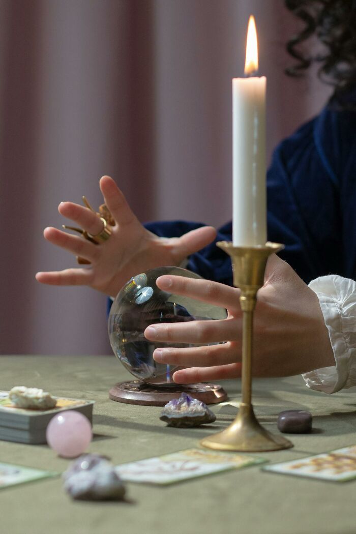 Person with rings using a crystal ball for psychic predictions with tarot cards and candle on the table