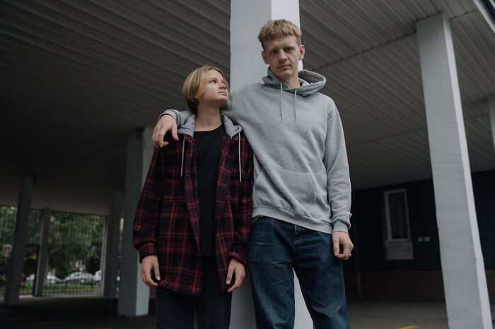 Two teenagers standing close under a roof, sharing a heartwarming moment and harmless secrets outdoors.