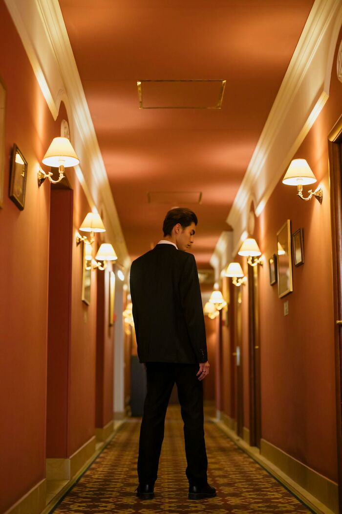 Man in a dark suit standing in a dimly lit hotel hallway, evoking night shift workers and chilling paranormal encounters.