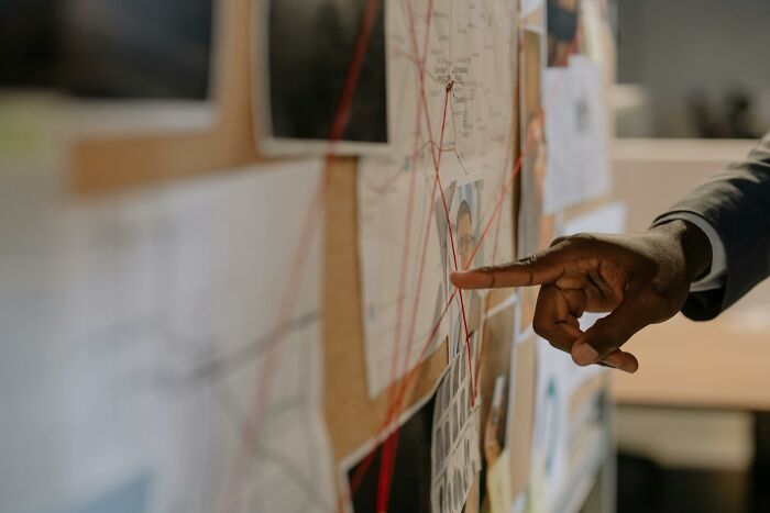 Person pointing at a timeline board with red strings connecting photos and notes, illustrating tiny human mistakes.
