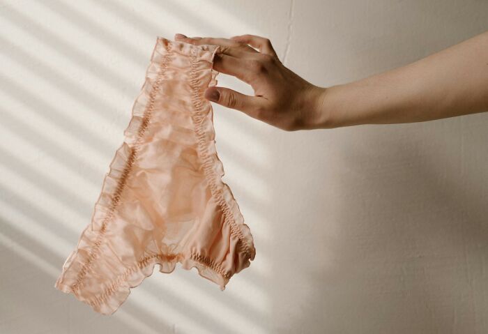 Hand holding sheer lingerie underwear in natural light, representing NSFW moments and personal online confessions.