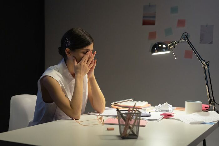 Stressed woman sitting at desk with documents and lamp, illustrating signs of talking to a psychopath during conversation.