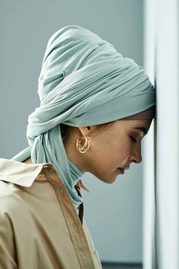 Young woman wearing a headscarf and gold hoop earrings, reflecting quietly, representing heartwarming secrets concept.
