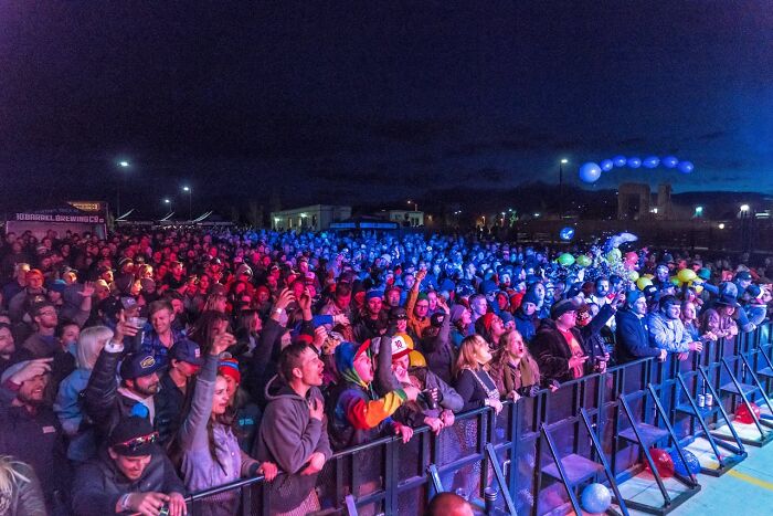 Crowd gathered at an outdoor nighttime event with colorful lights, capturing moments of people surviving crazy situations.