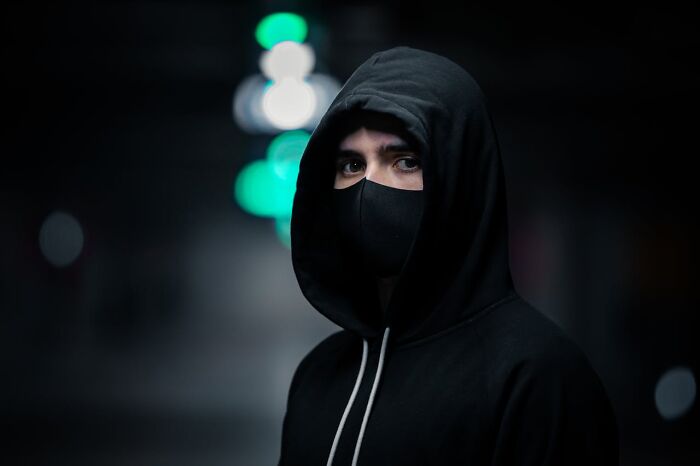Person wearing black hoodie and face mask in dark setting, representing people surviving crazy situations.