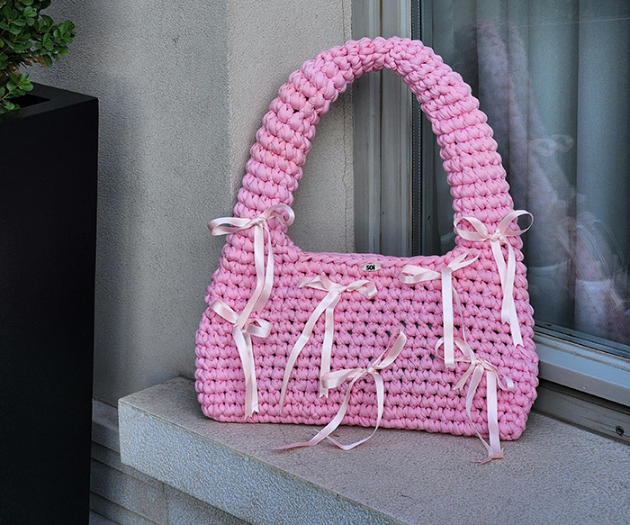 Pink knitted bag with ribbon details placed on a ledge, relating to the story about grieving son and burning bag conflict.
