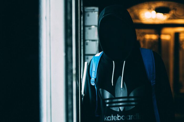 Mysterious hooded figure in dark setting wearing backpack, representing one of the world’s greatest unsolved mysteries.