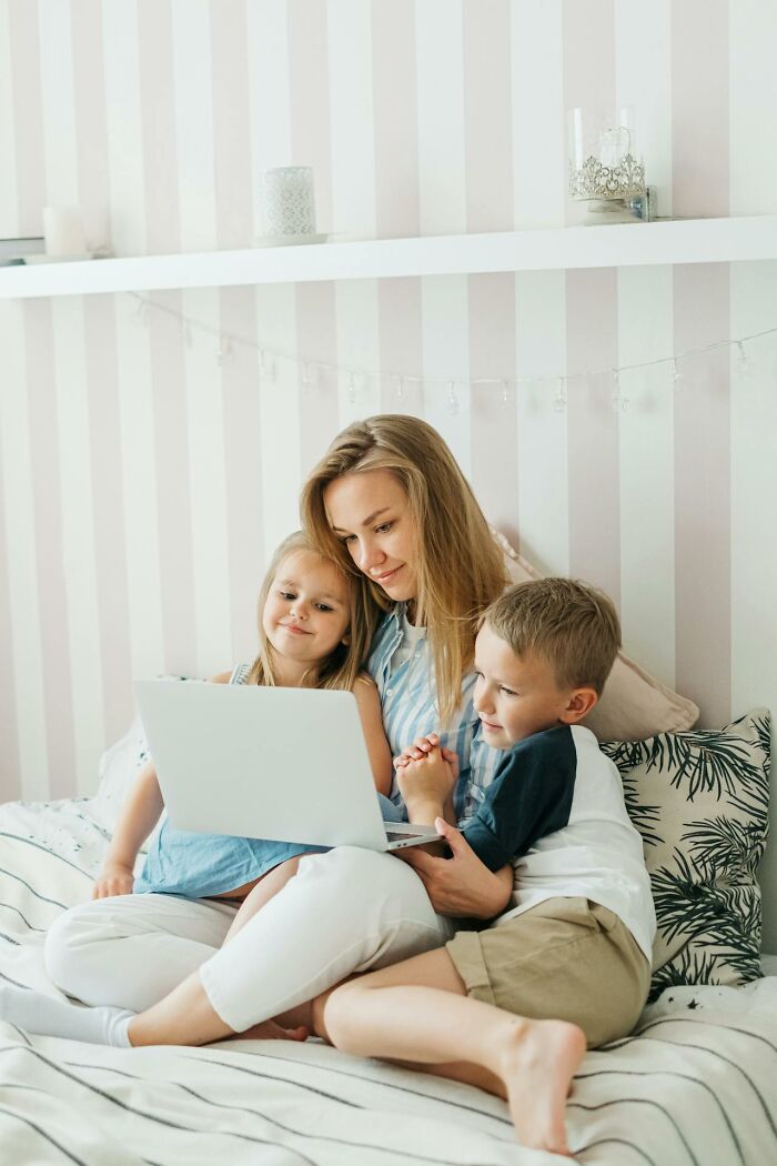 Mother with two children sitting on bed, looking at laptop, illustrating people experiencing things their psychics predicted.