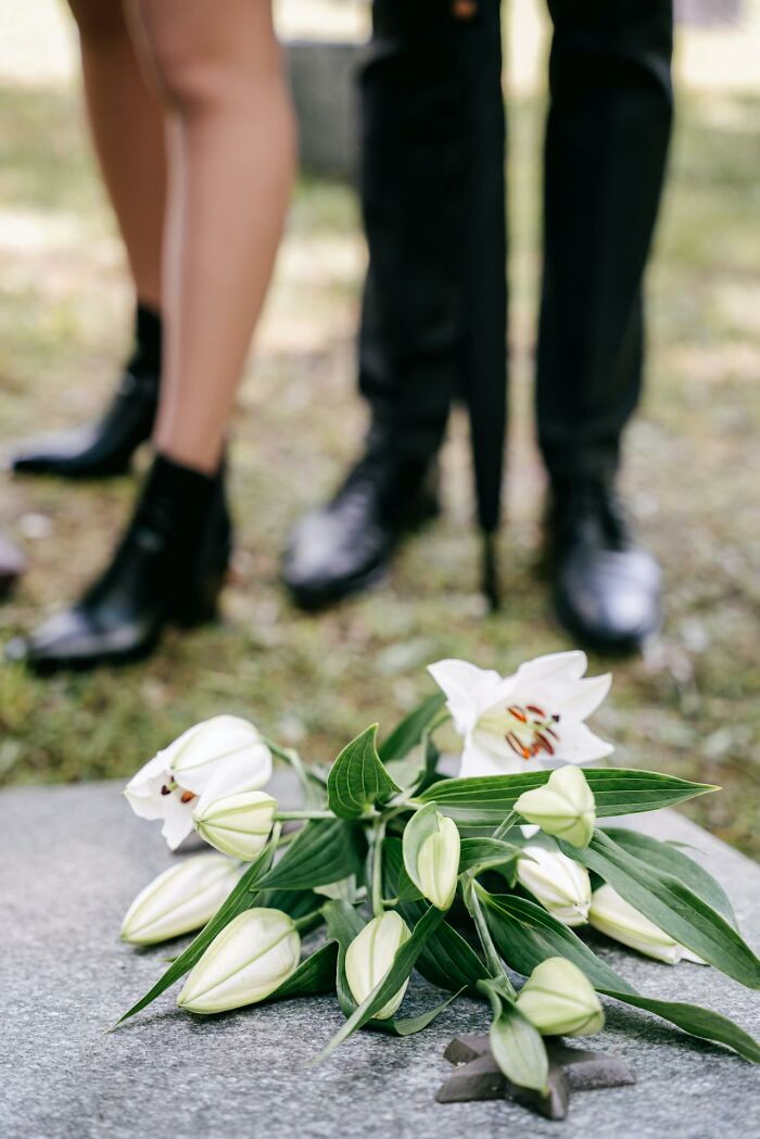 Bouquet of white lilies on a grave with adults standing nearby, evoking creepy and terrifying experiences with imaginary friends.