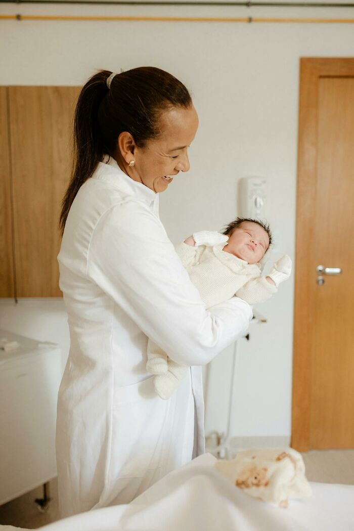 Smiling woman in white lab coat holding a newborn baby in a hospital room, representing talking to a psychopath concept.