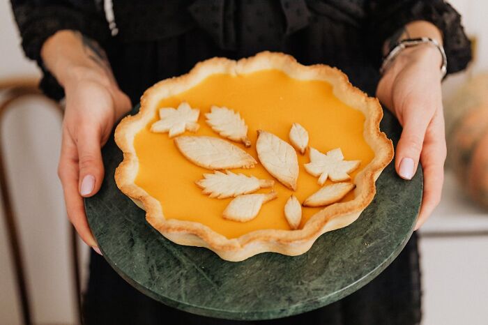 Person holding a homemade pumpkin pie with leaf-shaped crust decorations, representing heartwarming secret moments.