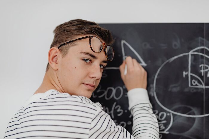 Young man with glasses on head writing math equations on a chalkboard symbolizing harmless secrets being revealed.