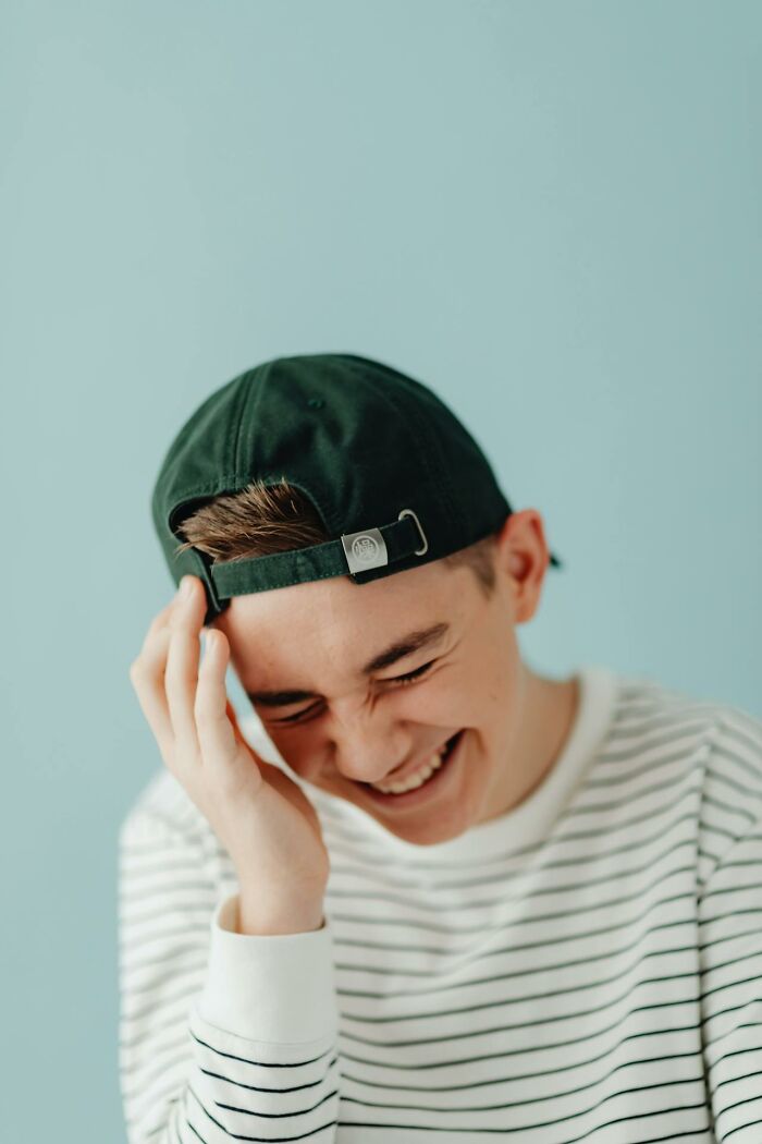 Teen boy in striped shirt and backwards cap smiling with hand on head, relating to creepy imaginary friends experiences.