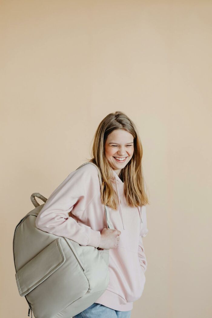 Adolescente sonriente con mochila gris, capturada en momento espontáneo, reflejando curiosidad de padres cotillas.