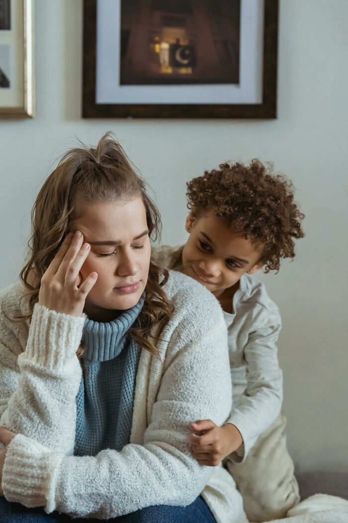 Woman with stressed expression holding her head while a child with a curious look stands behind her, illustrating signs of psychopath.