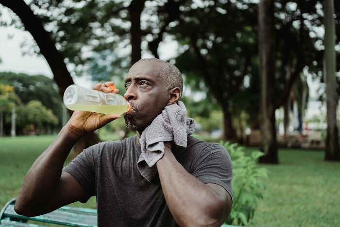 Middle-aged man drinking water and wiping sweat during outdoor exercise, showcasing cool facts about the human body.