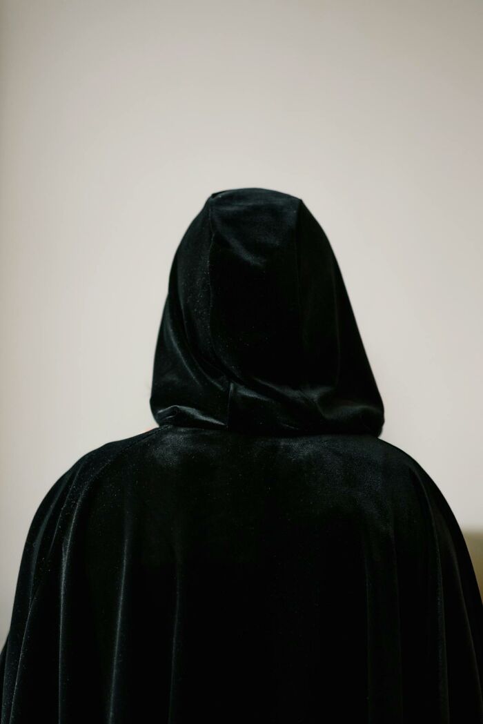 Person wearing a black hooded cloak from behind, evoking mystery and paranormal vibes linked to night shift workers.