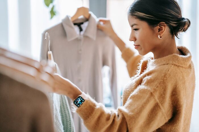 Young woman in a cozy sweater selecting clothes from a rack, illustrating heartwarming harmless secrets concept.