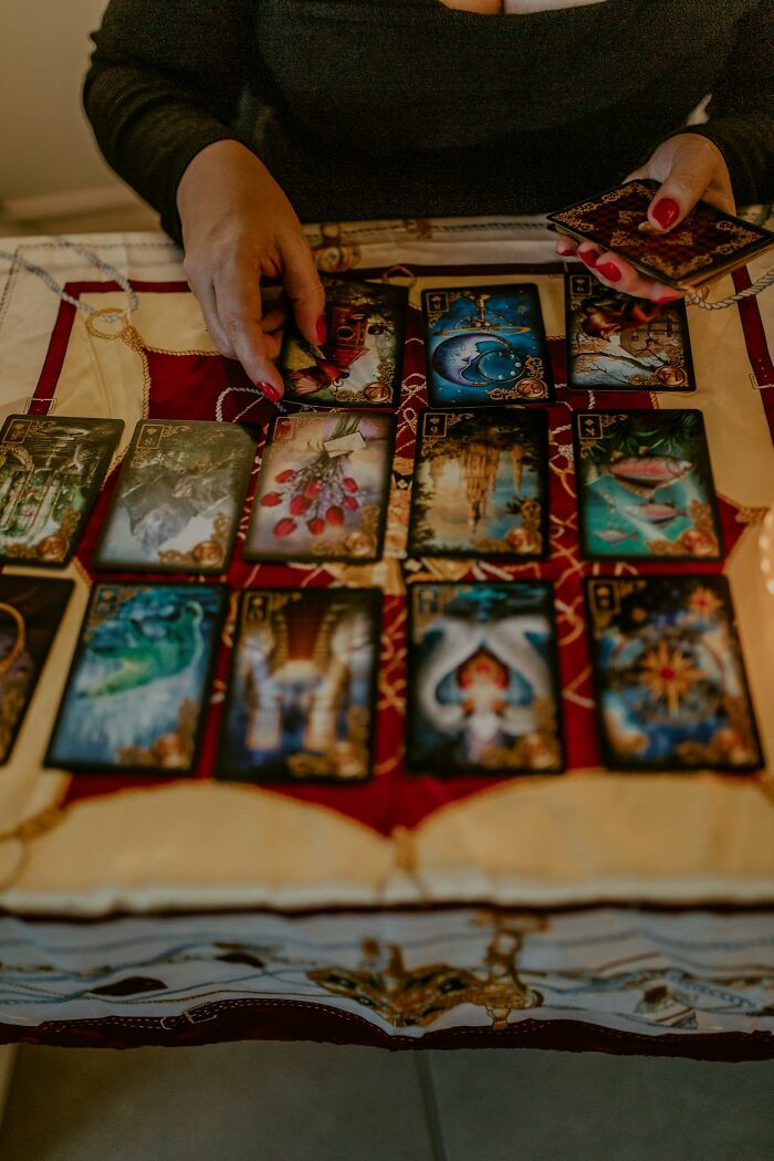 Person with red nails laying out tarot cards on a patterned cloth, illustrating psychic predictions being experienced.