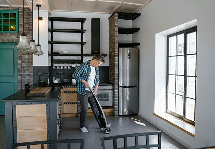 Man vacuuming in modern kitchen inside home, suggesting unexpected glimpse into perfect man's living space.