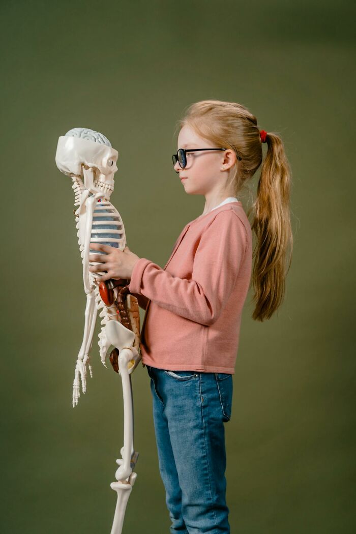 Young girl wearing glasses holding a skeleton model, illustrating creepy and terrifying experiences with imaginary friends