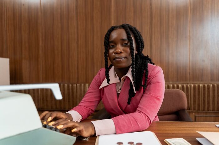 Woman in a pink suit typing on a typewriter at a desk, illustrating job interview red flags in a toxic workplace setting