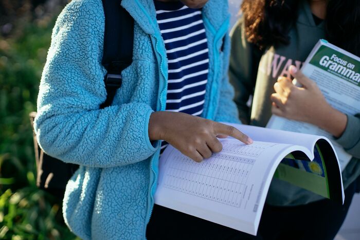 Two students outdoors studying grammar and sentence errors, one pointing to a page in an open workbook.