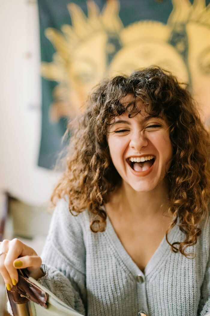 Young woman with curly hair laughing indoors, reflecting creepy and terrifying experiences parents had with kids imaginary friends.
