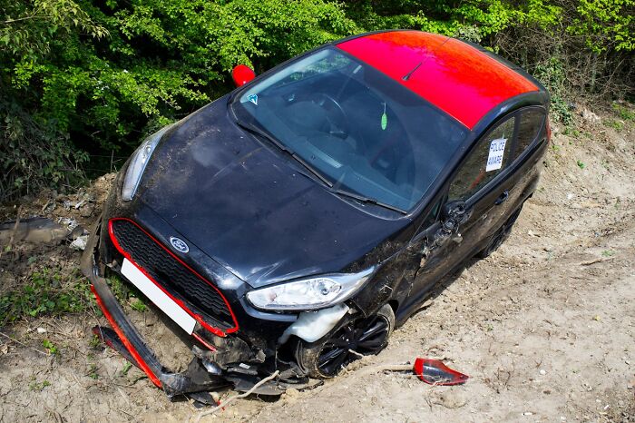 Damaged black and red car stuck in dirt after an accident, illustrating survival in crazy situations.