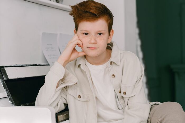 Red-haired teen boy with freckles wearing a beige jacket, sitting and sharing heartwarming harmless secrets indoors.
