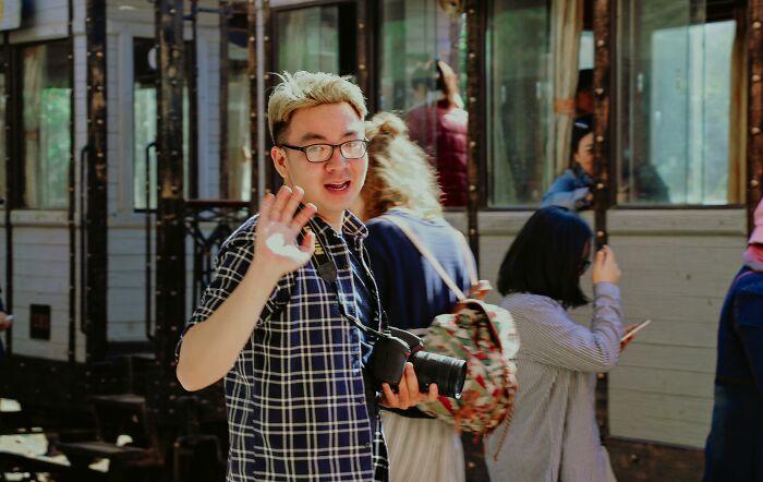 Young man with glasses holding a camera outdoors, representing people sharing ways to avoid babysitting online.