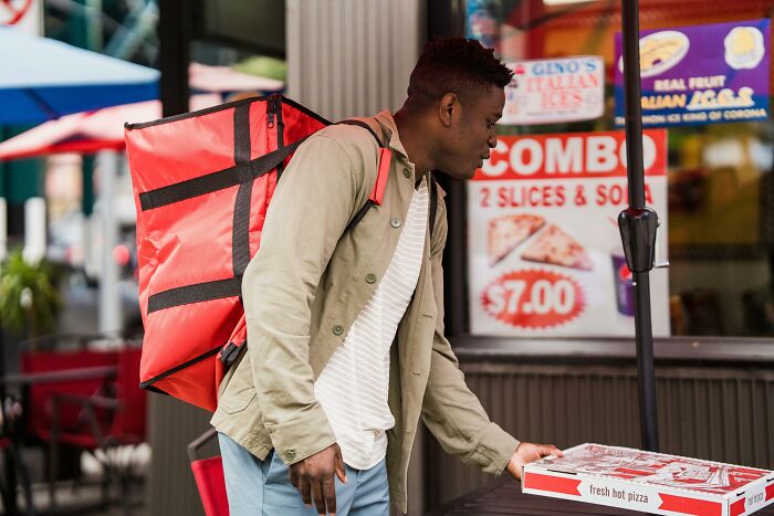 Young delivery worker picking up a pizza box outside a restaurant, illustrating reasons employees skipped their work day.