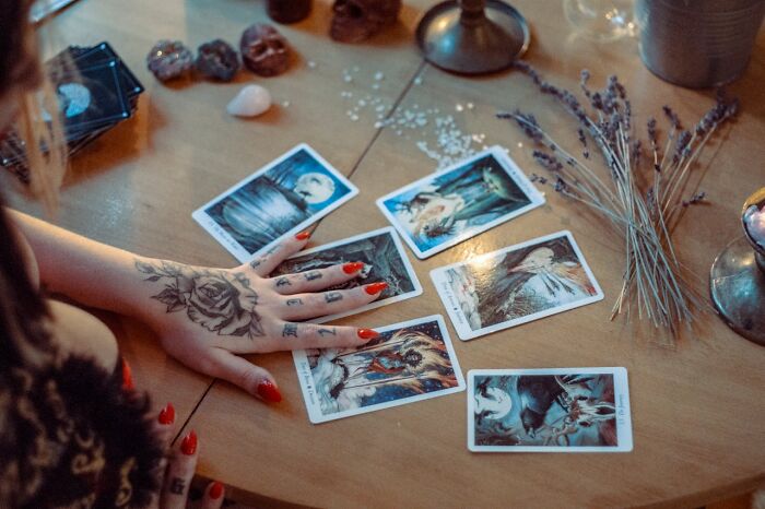 Fortune teller with red nails and a tattooed hand laying out tarot cards, illustrating psychic predictions coming true.