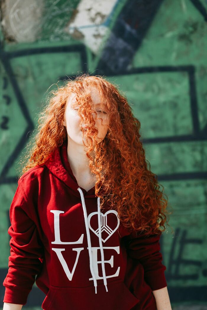 Young woman with curly red hair wearing a red LOVE hoodie standing against a green graffiti wall in a psychic prediction context