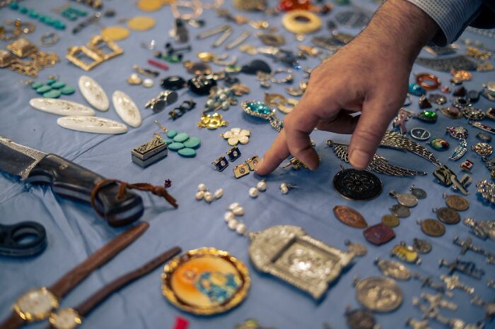 Hand pointing at vintage jewelry and trinkets laid out on a blue cloth, revealing hidden secrets and stories.