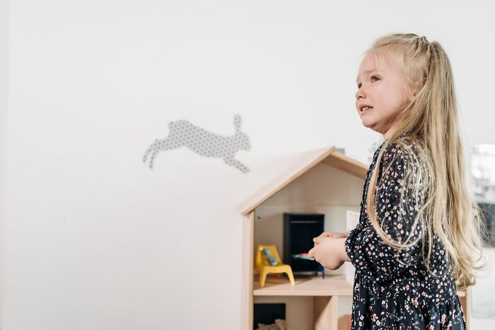 Young girl with long blonde hair playing with a dollhouse, capturing heartwarming and harmless secrets in childhood moments.