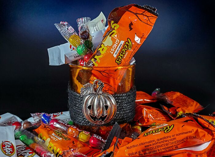 Glass filled with Halloween candy including Reese's, surrounded by assorted candy wrappers representing tiny human mistakes.