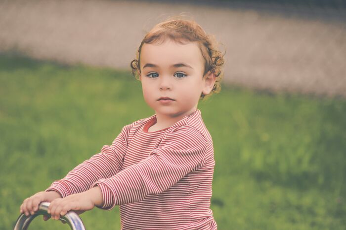 Toddler with curly hair in striped shirt outdoors, representing babysitting avoidance stories shared online.