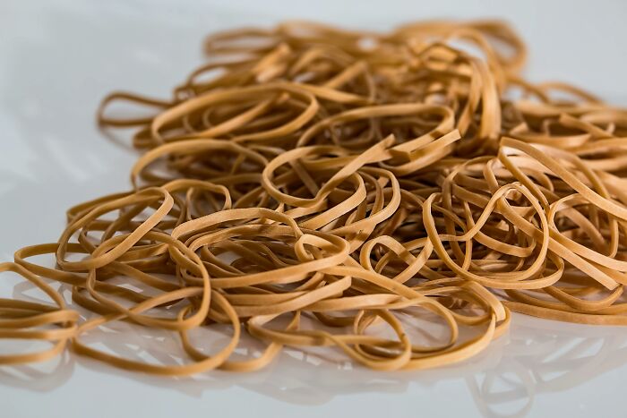 A close-up of tangled rubber bands scattered on a white surface representing tiny human mistakes impacting history.
