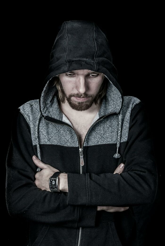 Man in a hooded jacket with folded arms looking down, illustrating signs of talking to a psychopath concept.