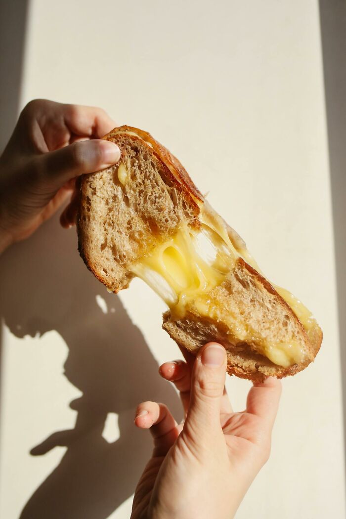 Hands pulling apart a grilled cheese sandwich with melted cheese stretching, illustrating heartwarming harmless secrets.