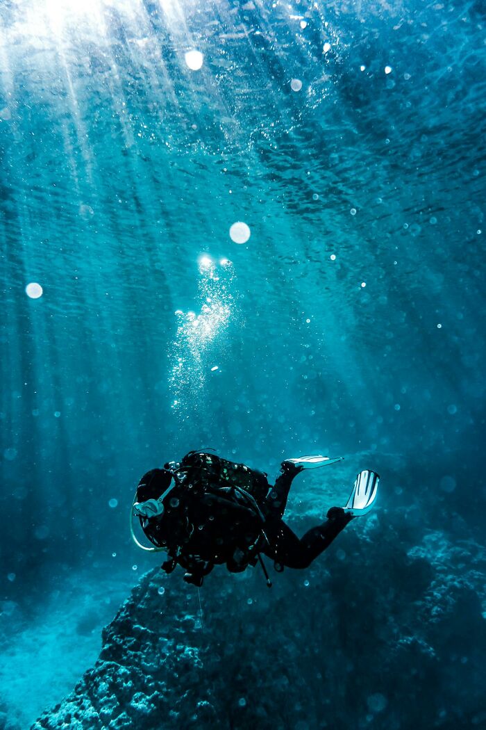 Scuba diver exploring deep ocean, surrounded by bubbles and sun rays, illustrating people surviving crazy situations underwater.