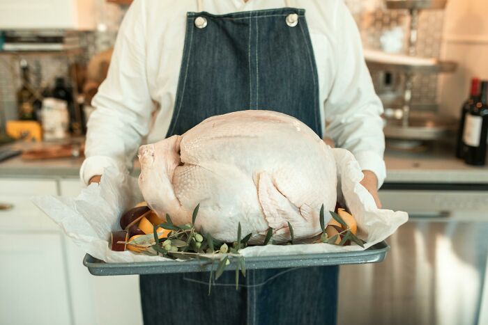 Person in dark apron holding a raw turkey in a kitchen, illustrating employees skipping work for insane reasons