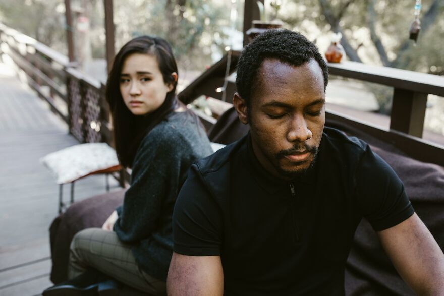 A conflicted couple sitting apart on a wooden bench outdoors, showing emotional tension and soul ties strain.
