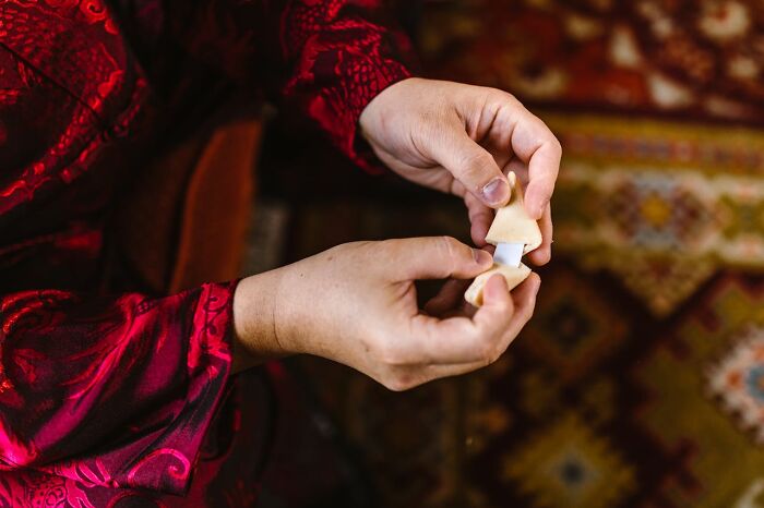 Person wearing a red patterned sleeve holding a small, carved wooden object against a colorful patterned background.
