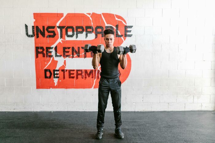 Person lifting dumbbells in a gym with a wall sign about resilience and determination, symbolizing coping with tough times.